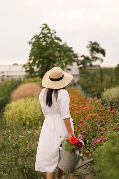 Красива брюнетка дівчина в білій сукні і капелюх з поливом може поливати квіти — стокове фото