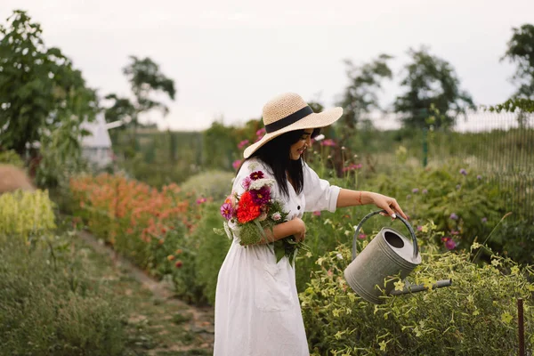 Красива брюнетка дівчина в білій сукні і капелюх з поливом може поливати квіти — стокове фото