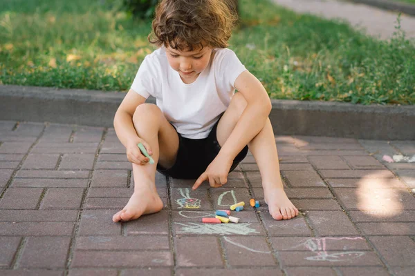 Маленький дошкольник рисует яркими мелом на земле. — стоковое фото