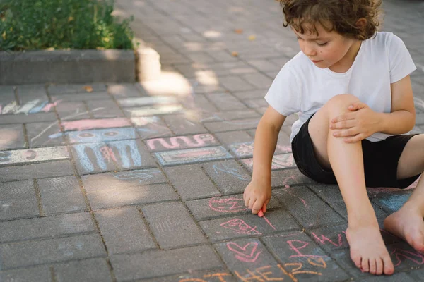 Pequeño niño preescolar dibuja con tiza de colores en el suelo. —  Fotos de Stock