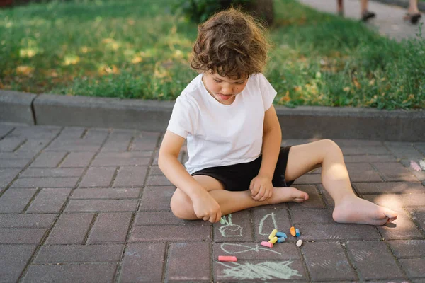 Маленький дошкольник рисует яркими мелом на земле. — стоковое фото