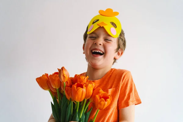 Funny boy with orange tulips and in the mask of a chick on white background. — Stock Photo, Image