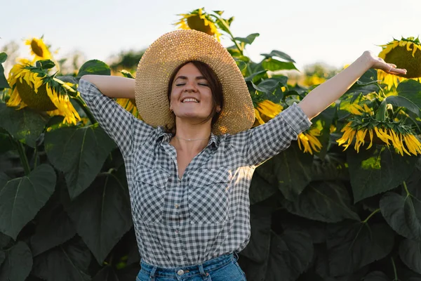 Красива молода жінка з соняшниками насолоджується природою і сміється на літньому соняшниковому полі . — стокове фото