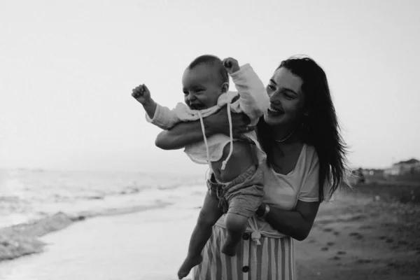 Foto em preto e branco. Feliz dia das mães. Bela mãe e bebê brincam na praia. — Fotografia de Stock