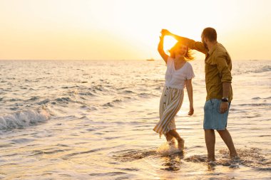 Young romantic couple dancing turning around by sea. Seascape at sunset with beautiful sky