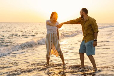 Young romantic couple dancing turning around by sea. Seascape at sunset with beautiful sky
