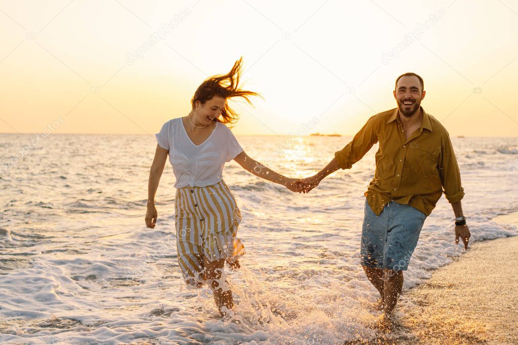 Young romantic couple dancing turning around by sea. Seascape at sunset with beautiful sky