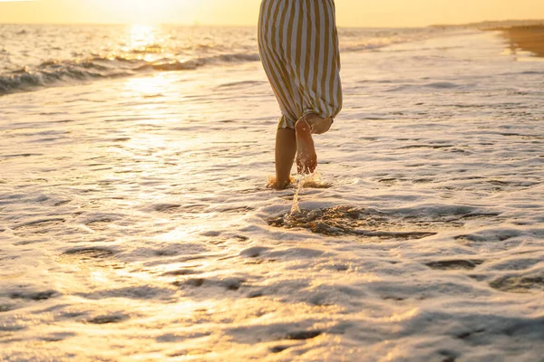 Sarı dalgalı bir elbiseyle denizde dans eden genç ve mutlu bir kadın..