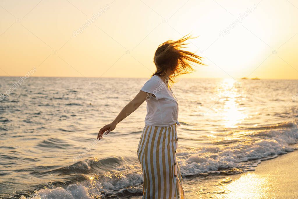 Young happy woman dancing turning around by sea in a yellow fluttering dress.