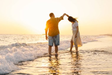 Young romantic couple dancing turning around by sea. Seascape at sunset with beautiful sky
