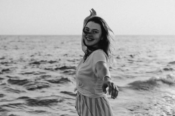 Black and white photo. Young happy woman dancing turning around by sea in a yellow fluttering dress. — стоковое фото