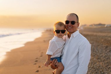 Baba ve bebek kumsalda oynuyorlar. Babam ve o gün batımının tadını çıkarıyorlar..