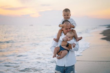Baba ve çocuklar sahilde oynuyorlar. Babam ve o gün batımının tadını çıkarıyorlar..