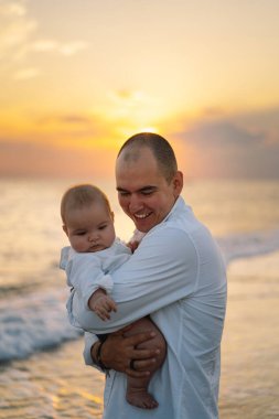 Baba ve bebek kumsalda oynuyorlar. Babam ve o gün batımının tadını çıkarıyorlar..