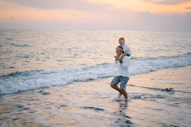 Baba ve bebek kumsalda oynuyorlar. Babam ve o gün batımının tadını çıkarıyorlar..