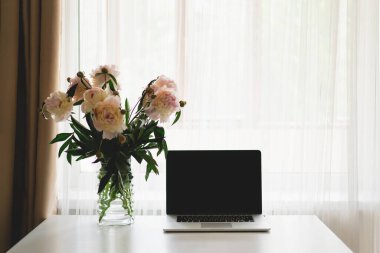 Spring Home Ofisi hala yaşam kompozisyonu. Laptop ve vazo. Masasında pembe şakayık çiçekleri olan bir vazo. Konforlu ofis