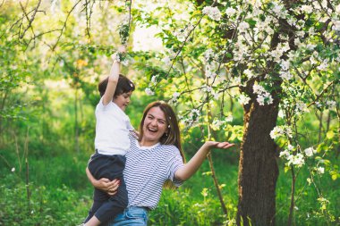 Anne ve küçük oğlu bahar bahçesinde altın saat boyunca. Anne ve oğlu doğada aktiftir. Aile bir bahar bahçesinde yürüyor. Anneler günün kutlu olsun.