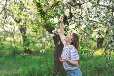 Bahar çiçekleriyle güzel genç bir kadın doğanın tadını çıkarıyor ve bahar bahçesinde gülüyor. Elma ağacının dalını tutan kadın. Özgürlük ve mutluluk kavramı. İlkbahar.