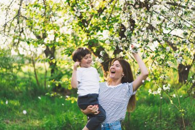 Anne ve küçük oğlu bahar bahçesinde altın saat boyunca. Anne ve oğlu doğada aktiftir. Aile bir bahar bahçesinde yürüyor. Anneler günün kutlu olsun.