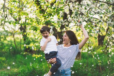 Anne ve küçük oğlu bahar bahçesinde altın saat boyunca. Anne ve oğlu doğada aktiftir. Aile bir bahar bahçesinde yürüyor. Anneler günün kutlu olsun.