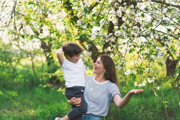 Mother with little baby son in spring garden during golden hour. Mom and son are active in nature. Family walks in a spring garden. Happy mothers day