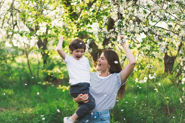 Mother with little baby son in spring garden during golden hour. Mom and son are active in nature. Family walks in a spring garden. Happy mothers day