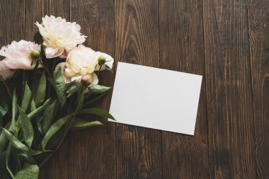 Beyaz buket pembe şakayık çiçekleri ve tahta arka planda beyaz kart. Minimalist estetik şakayıklar yatıyordu. Anneler Günü ya da Kadınlar Günü için güzel bir kart