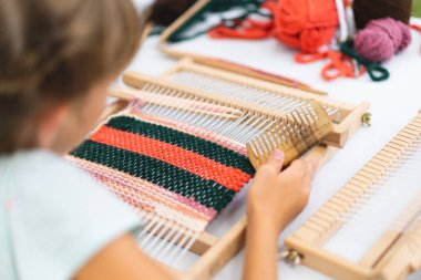 Üstat sınıfında örgü ören küçük bir halı ören kız. Kız manuel masa tezgahında nasıl örüleceğini öğreniyor. Yaradılış süreci. El yapımı konsept