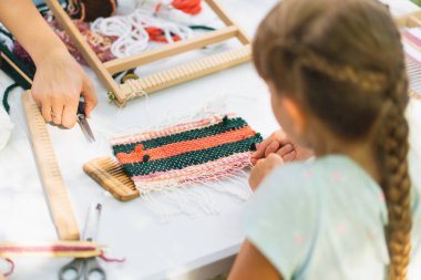Üstat sınıfında örgü ören küçük bir halı ören kız. Kız manuel masa tezgahında nasıl örüleceğini öğreniyor. Yaradılış süreci. El yapımı konsept