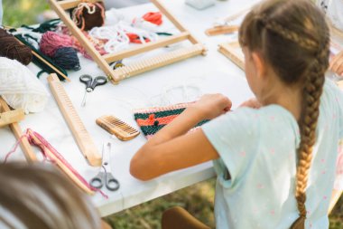 Üstat sınıfında örgü ören küçük bir halı ören kız. Kız manuel masa tezgahında nasıl örüleceğini öğreniyor. Yaradılış süreci. El yapımı konsept