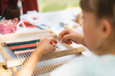 Üstat sınıfında örgü ören küçük bir halı ören kız. Kız manuel masa tezgahında nasıl örüleceğini öğreniyor. Yaradılış süreci. El yapımı konsept