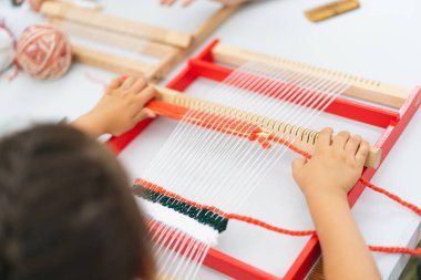 Girl weaving small rug with pattern at masterclass on weaving. Girl is studying how to weave on manual table loom. Process of creation. Handmade concept