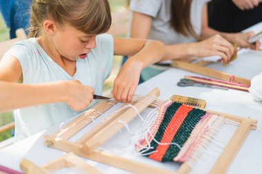 Üstat sınıfında örgü ören küçük bir halı ören kız. Kız manuel masa tezgahında nasıl örüleceğini öğreniyor. Yaradılış süreci. El yapımı konsept