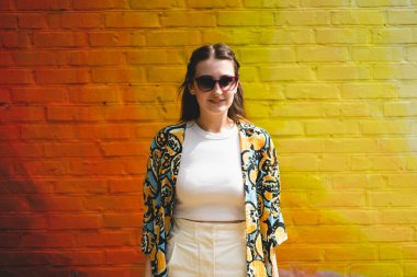 Renkli turuncu arka planda güneş gözlüklü mutlu genç bir kadının yaz portresi.