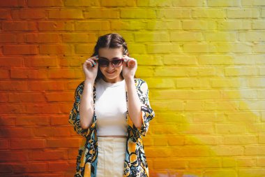 Summer portrait of happy smiling young woman with sunglass on colorful orange background
