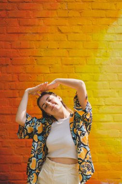 Renkli turuncu arka planda güneş gözlüklü mutlu genç bir kadının yaz portresi.