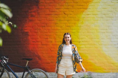 Renkli turuncu arka planda güneş gözlüklü mutlu genç bir kadının yaz portresi.