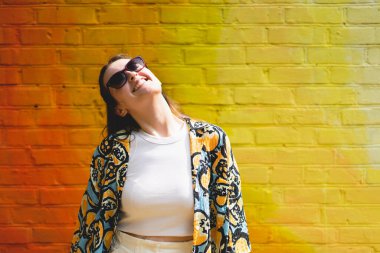 Renkli turuncu arka planda güneş gözlüklü mutlu genç bir kadının yaz portresi.