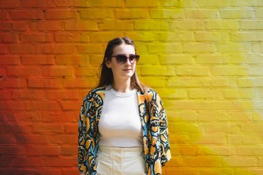 Renkli turuncu arka planda güneş gözlüklü mutlu genç bir kadının yaz portresi.