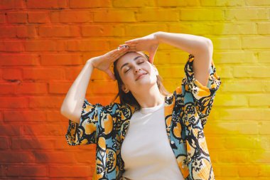 Renkli turuncu arka planda güneş gözlüklü mutlu genç bir kadının yaz portresi.