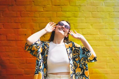 Renkli turuncu arka planda güneş gözlüklü mutlu genç bir kadının yaz portresi.