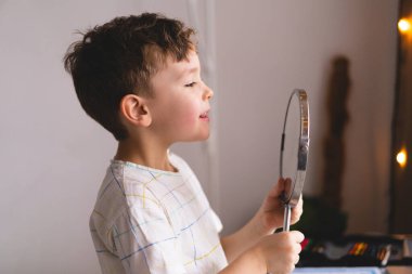 Konuşma terapisi konsepti. Sesi telaffuz eden şirin küçük çocuk aynaya bakıp dizüstü bilgisayarla konuşma terapisi dersi veriyor.