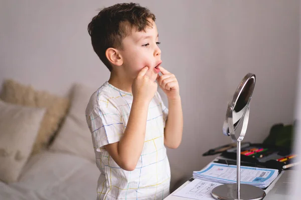 Speech therapy concept. Cute little boy pronouncing sound O looking at mirror doing an online Speech therapy lesson through a laptop