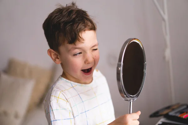 Speech therapy concept. Cute little boy pronouncing sound O looking at mirror doing an online Speech therapy lesson through a laptop