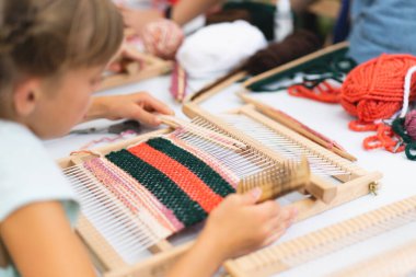 Üstat sınıfında örgü ören küçük bir halı ören kız. Kız manuel masa tezgahında nasıl örüleceğini öğreniyor. Yaradılış süreci. El yapımı konsept