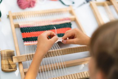 Üstat sınıfında örgü ören küçük bir halı ören kız. Kız manuel masa tezgahında nasıl örüleceğini öğreniyor. Yaradılış süreci. El yapımı konsept