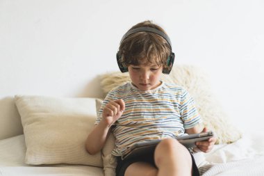 Evdeki yatakta uzanıp bilgisayar tabletleriyle oynayan, internetten kitap okuyan ve kablosuz kulaklıkla müzik dinleyen tatlı çocuk.