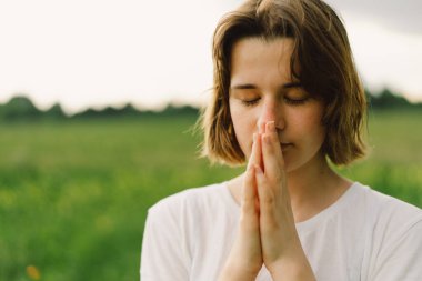 Teenager Girl closed her eyes, praying. Hands folded in prayer concept for faith, spirituality and religion. Peace, hope, dreams concept
