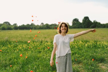 Portrait Of Teenage Girl. Happy Cheerful Teen Girl With Pronounced Face dancing In Outdoors in a field with red poppies.