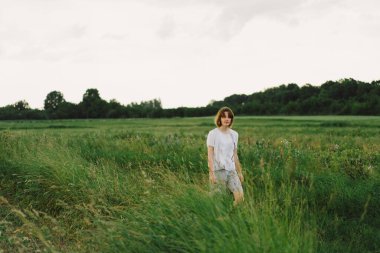 Beautiful teenager girl on the field in green grass and blowing dandelion. Outdoors. Enjoy Nature. Healthy Smiling Girl on summer lawn. Allergy free concept.